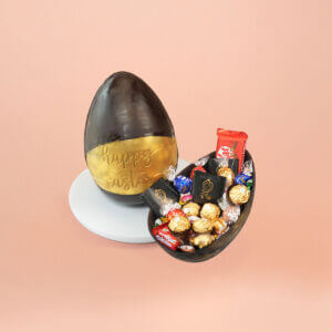 Dark chocolate Easter egg with a golden band and "Happy Easter" message, paired with a chocolate shell filled with KitKat, Ferrero Rocher, and assorted luxury candies – CakeSquare gift box.