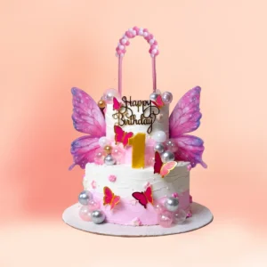 Two tier pink and white butterfly first birthday cake for girls in Chennai with large pink wings, a pearl balloon arch topper and a gold number one from Cake Square.