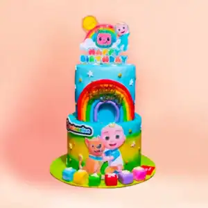 Two tier CoComelon theme birthday cake in Chennai with a fondant rainbow arch, the character and his puppy, alphabet blocks at the base and a rainbow topper from Cake Square.