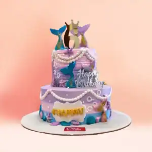 Two tier lilac mermaid theme birthday cake for girls in Chennai with pearl garlands, blue and gold mermaid tails, starfish, shells and a gold crown number topper from Cake Square.