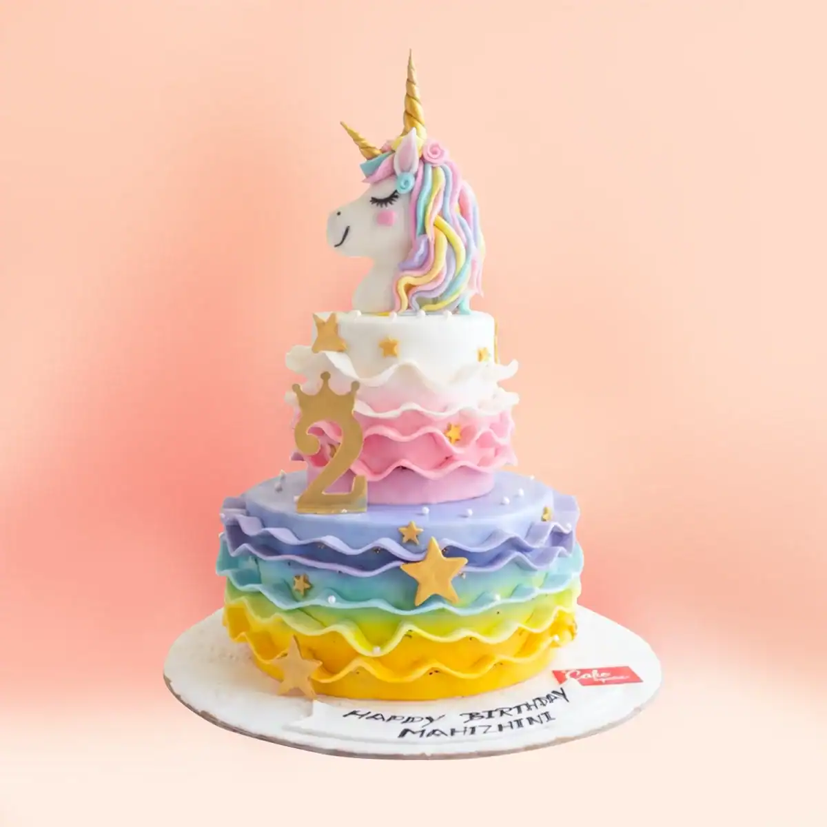 Two tier unicorn theme birthday cake in Chennai with a fondant unicorn head topper, rainbow ruffles from yellow to purple, gold stars and a crown number from Cake Square.