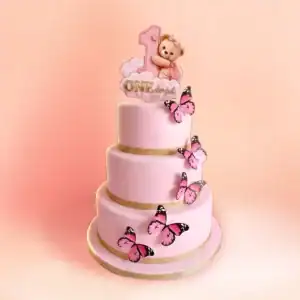 Three tier pink teddy bear first birthday cake for girls in Chennai with a teddy hugging a gold number one, a ONE plaque and pink butterflies from Cake Square.