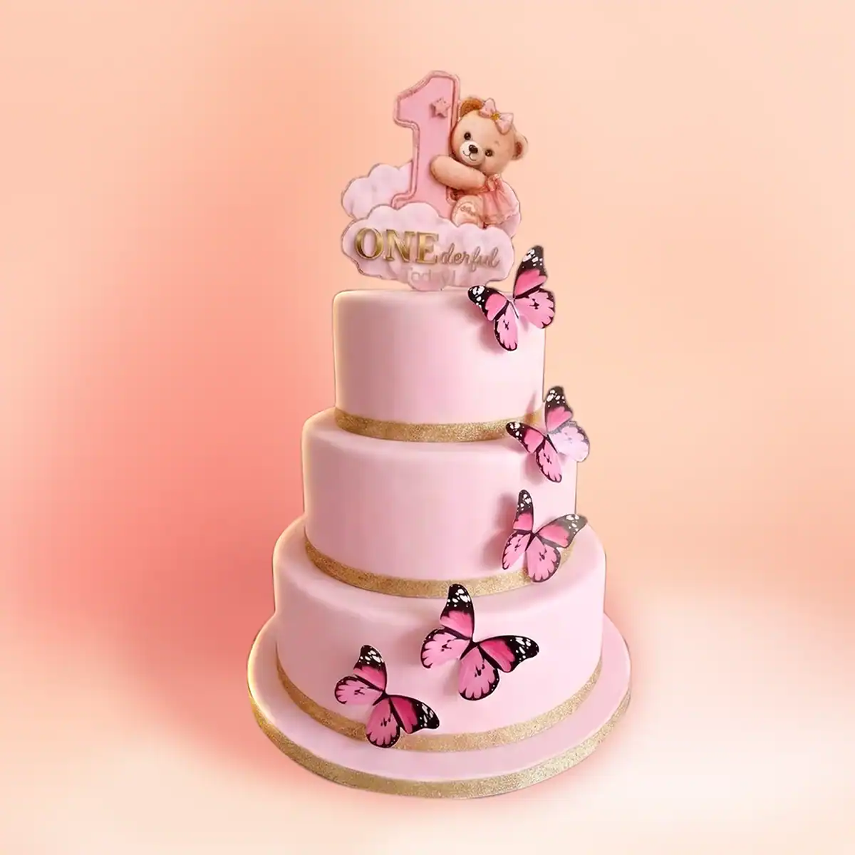 Three tier pink teddy bear first birthday cake for girls in Chennai with a teddy hugging a gold number one, a ONE plaque and pink butterflies from Cake Square.