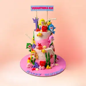 Two tier Baby Shark theme first birthday cake for girls in Chennai with a pink ocean design, shark and sea creature figures and a custom name banner from Cake Square.