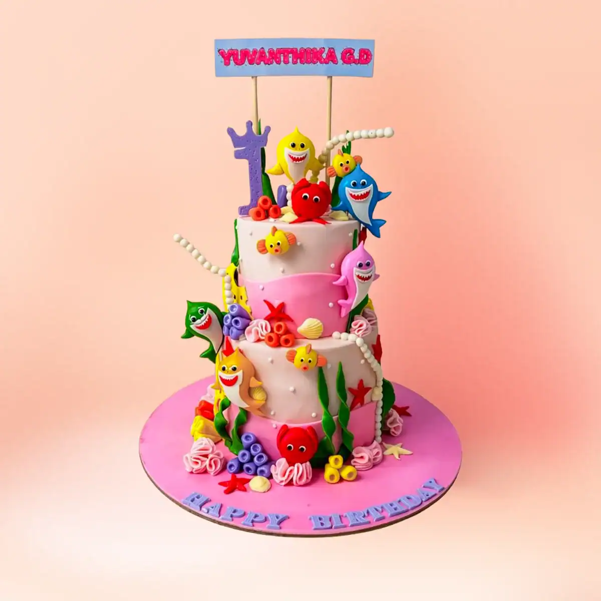 Two tier Baby Shark theme first birthday cake for girls in Chennai with a pink ocean design, shark and sea creature figures and a custom name banner from Cake Square.