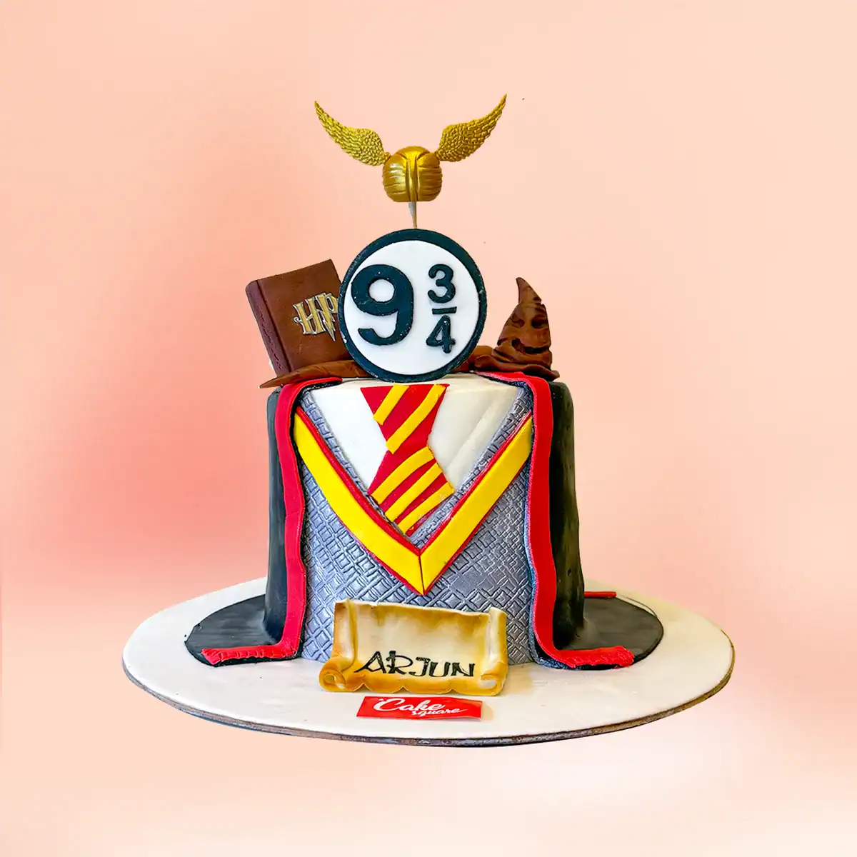 Harry Potter theme birthday cake in Chennai with a Gryffindor tie and cloak design, a Golden Snitch topper, Sorting Hat and Platform Nine and Three Quarters sign from Cake Square.