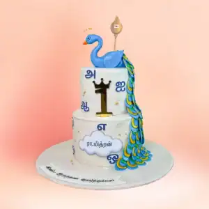 Two tier Murugan theme first birthday cake in Chennai with a blue peacock topper, gold vel and Tamil lettering, available fully eggless from Cake Square.