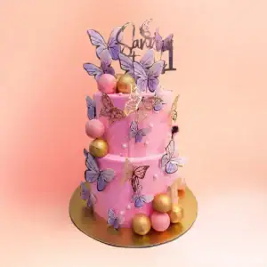 Two tier pink butterfly theme first birthday cake for girls in Chennai with purple and gold butterflies, sugar pearls and a custom name and number one topper from Cake Square.