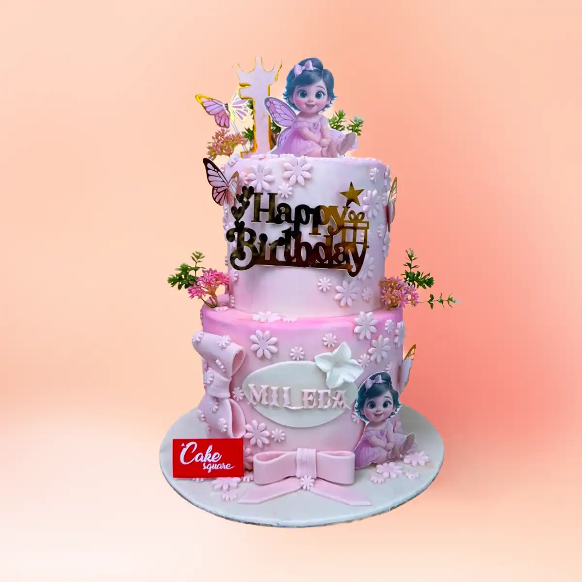 Two tier pink fairy theme first birthday cake for girls in Chennai with floral fondant work, fairy figures and a personalised name plaque and number one topper from Cake Square.