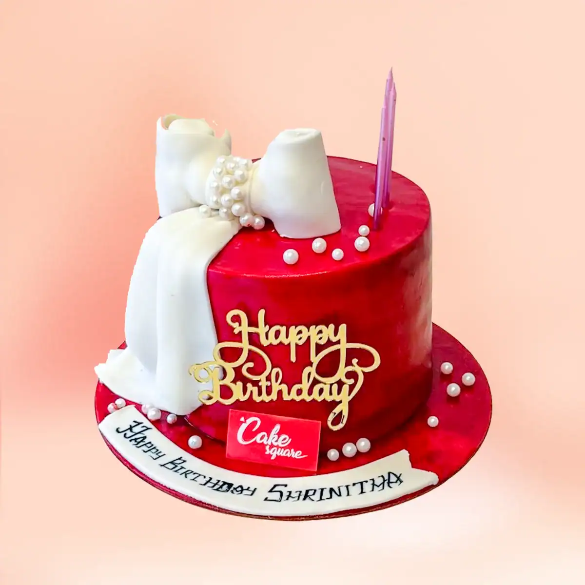 Red fondant luxury birthday cake in Chennai with a draped white fondant bow, pearl string detailing and a gold Happy Birthday topper from Cake Square.