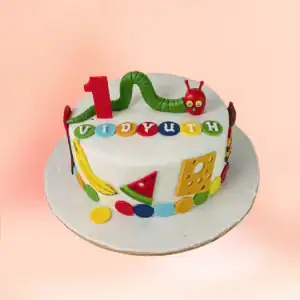 Very Hungry Caterpillar theme first birthday cake in Chennai with a green caterpillar figure, fondant fruit shapes and a custom name and number one topper from Cake Square.