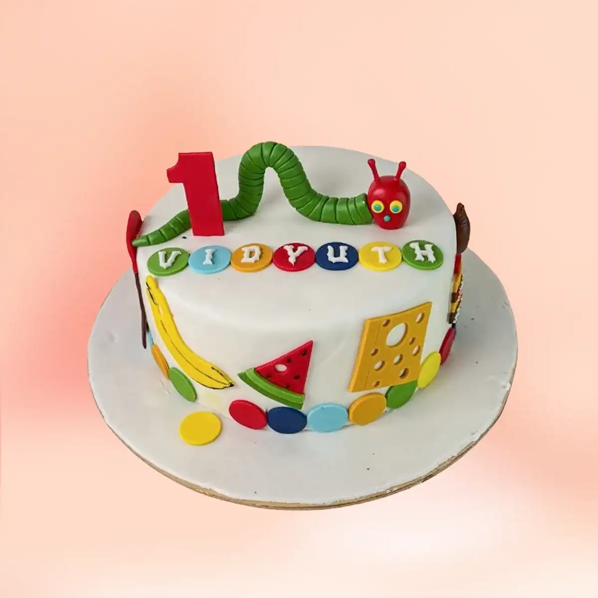 Very Hungry Caterpillar theme first birthday cake in Chennai with a green caterpillar figure, fondant fruit shapes and a custom name and number one topper from Cake Square.